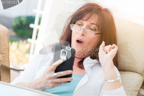 Image of Shocked Middle Aged Woman Gasps While Using Her Smart Phone
