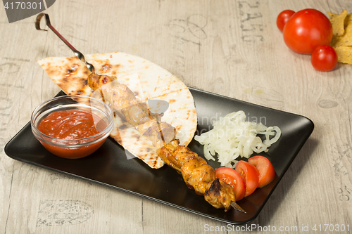 Image of shashlik. kebab skewer, black rectangular plate. sauce and onions