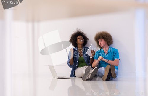 Image of multiethnic couple sitting on the floor with a laptop and tablet