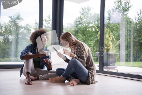 Image of multiethnic women sit on the floor and drinking coffee