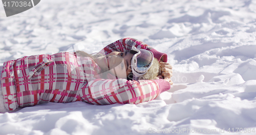 Image of Young woman lying on snow with ski goggles