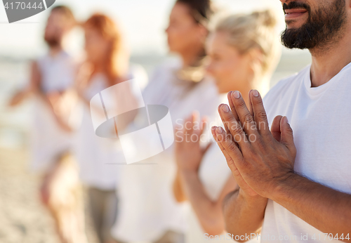 Image of group of people making yoga or meditating on beach