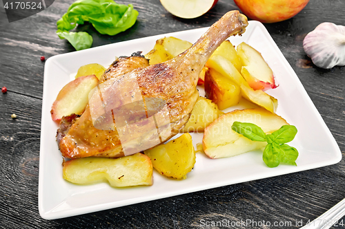 Image of Duck leg with apple and potatoes in plate on board
