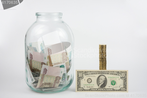 Image of Close to three-liter jar filled with money is a stack of coins next to it is a banknote of ten dollars