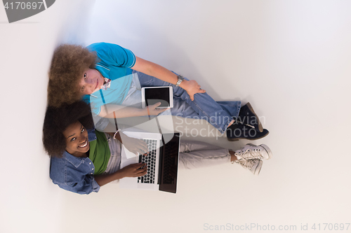 Image of multiethnic couple sitting on the floor with a laptop and tablet