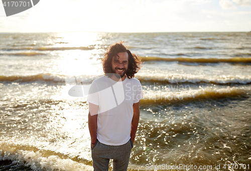 Image of happy man in white t-shirt on beach over sea