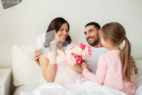 Image of happy girl giving flowers to mother in bed at home