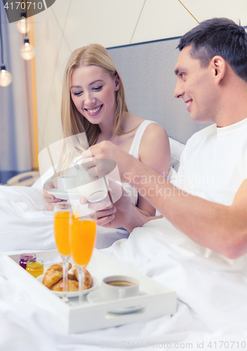 Image of smiling couple having breakfast in bed in hotel