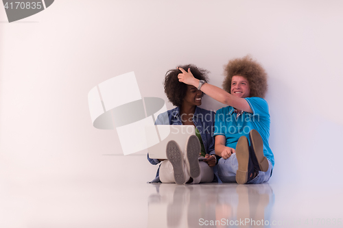 Image of multiethnic couple sitting on the floor with a laptop and tablet