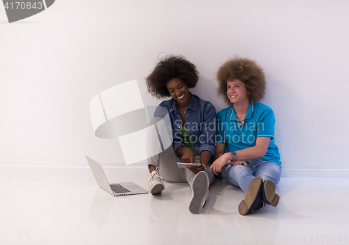 Image of multiethnic couple sitting on the floor with a laptop and tablet