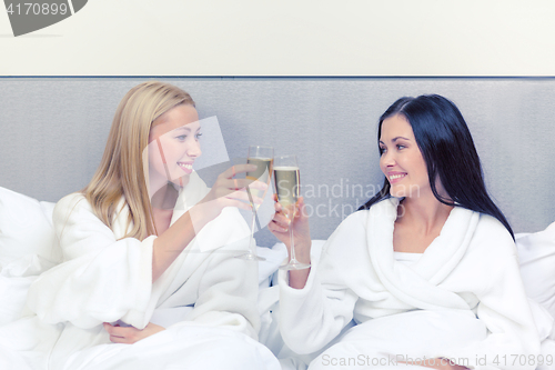 Image of smiling girlfriends with champagne glasses in bed