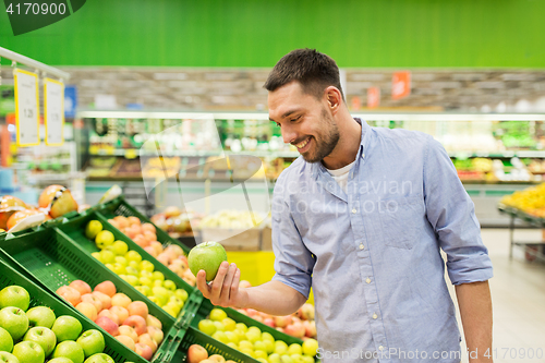 Image of happy man buying green apples at grocery store