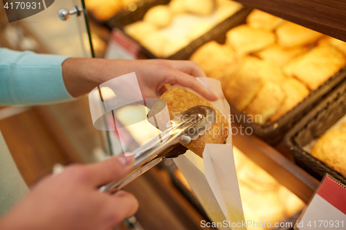 Image of hand with tongs taking bun at bakery or grocery