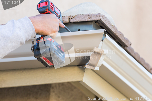 Image of Worker Attaching Aluminum Rain Gutter to Fascia of House.