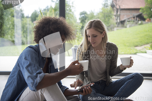 Image of multiethnic women sit on the floor and drinking coffee