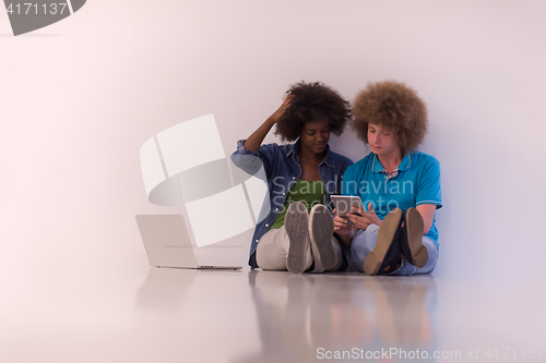 Image of multiethnic couple sitting on the floor with a laptop and tablet