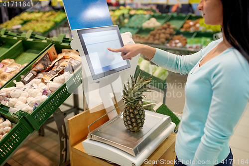 Image of woman weighing pineapple on scale at grocery store