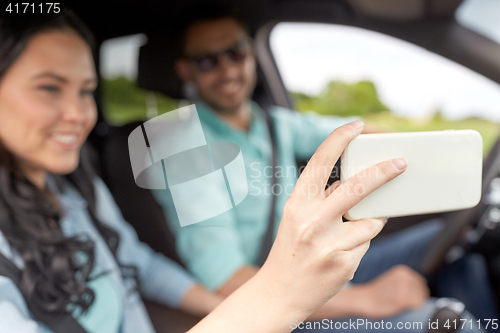 Image of couple driving in car and taking smartphone selfie