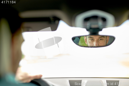 Image of rearview mirror reflection of man driving car