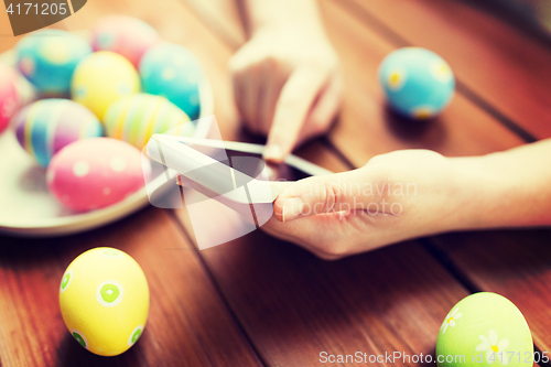 Image of close up of hands with easter eggs and smartphone