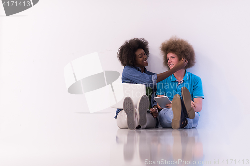 Image of multiethnic couple sitting on the floor with a laptop and tablet