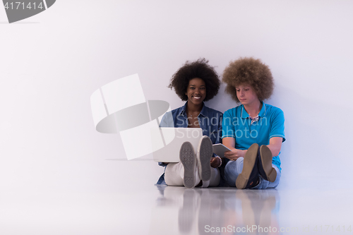 Image of multiethnic couple sitting on the floor with a laptop and tablet