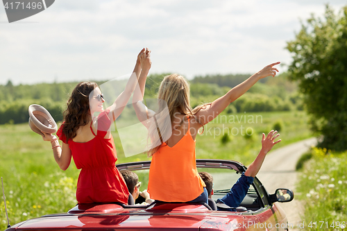 Image of happy friends driving in cabriolet car at country