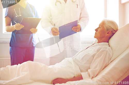 Image of doctor and nurse visiting senior woman at hospital