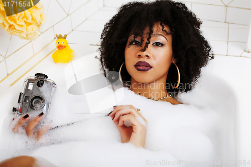 Image of young afro-american teen girl laying in bath with foam, wearing 