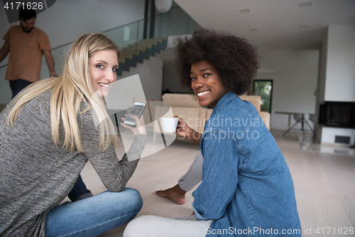 Image of young multiethnic women sit on the floor and drinking coffee