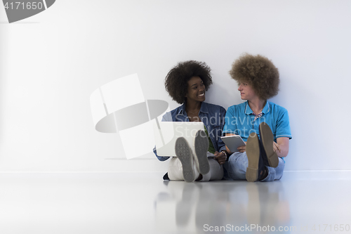 Image of multiethnic couple sitting on the floor with a laptop and tablet