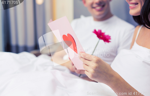 Image of close up of couple in bed with postcard and flower