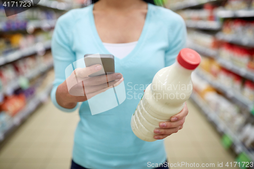 Image of woman with smartphone buying milk at supermarket