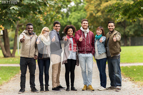 Image of happy friends showing thumbs up at autumn park