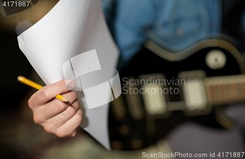 Image of man with guitar, pencil and paper at music studio