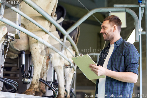 Image of man with clipboard and milking cows on dairy farm