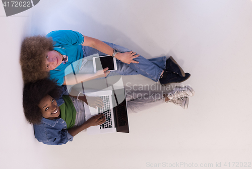 Image of multiethnic couple sitting on the floor with a laptop and tablet