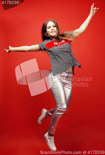 Image of young pretty emitonal posing teenage girl on bright red background jumping with flying hair, happy smiling lifestyle people concept 