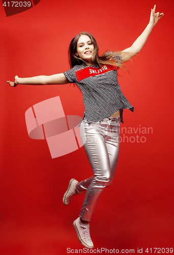 Image of young pretty emitonal posing teenage girl on bright red background jumping with flying hair, happy smiling lifestyle people concept 