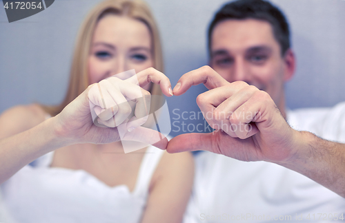 Image of smiling couple in bed making heart shape gesture