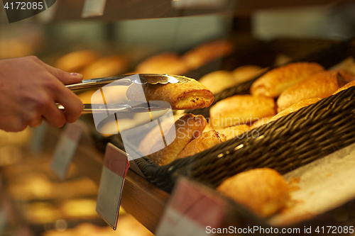 Image of hand with tongs taking bun at bakery or grocery