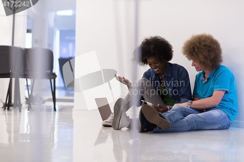 Image of multiethnic couple sitting on the floor with a laptop and tablet