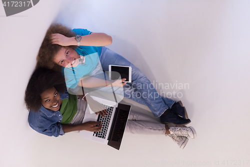 Image of multiethnic couple sitting on the floor with a laptop and tablet