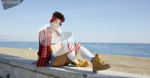 Image of Trendy young woman relaxing on a beachfront wall