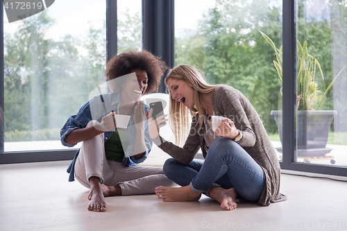 Image of multiethnic women sit on the floor and drinking coffee