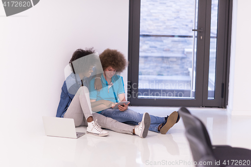 Image of multiethnic couple sitting on the floor with a laptop and tablet