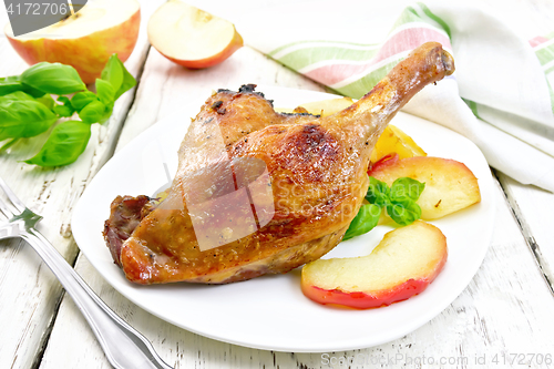 Image of Duck leg with apple in plate and napkin on board