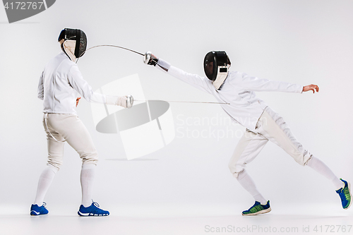 Image of The two men wearing fencing suit practicing with sword against gray