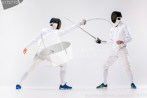 Image of The two men wearing fencing suit practicing with sword against gray