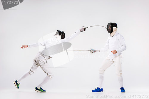 Image of The two men wearing fencing suit practicing with sword against gray